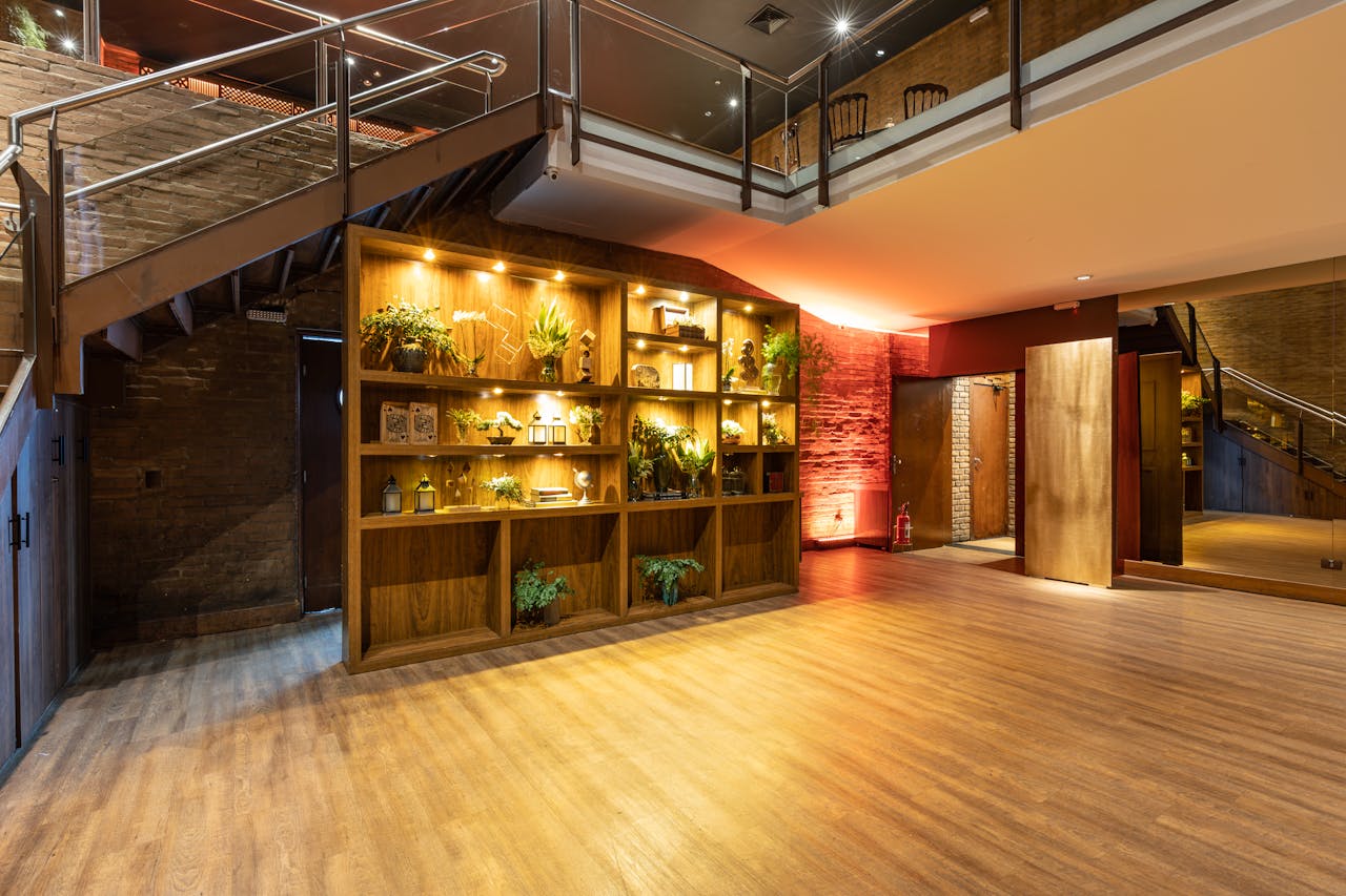 Contemporary indoor lobby featuring illuminated wooden shelving with plants and an iron staircase.